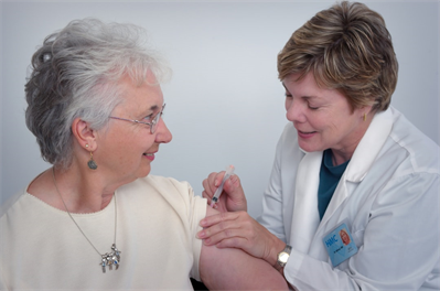 In this 2006 image, a qualified healthcare practitioner was in the process of administering an intramuscular immunization to a middle-aged woman, using the woman’s left shoulder muscle as the injection site. The practitioner immobilized the injection area with her free hand.